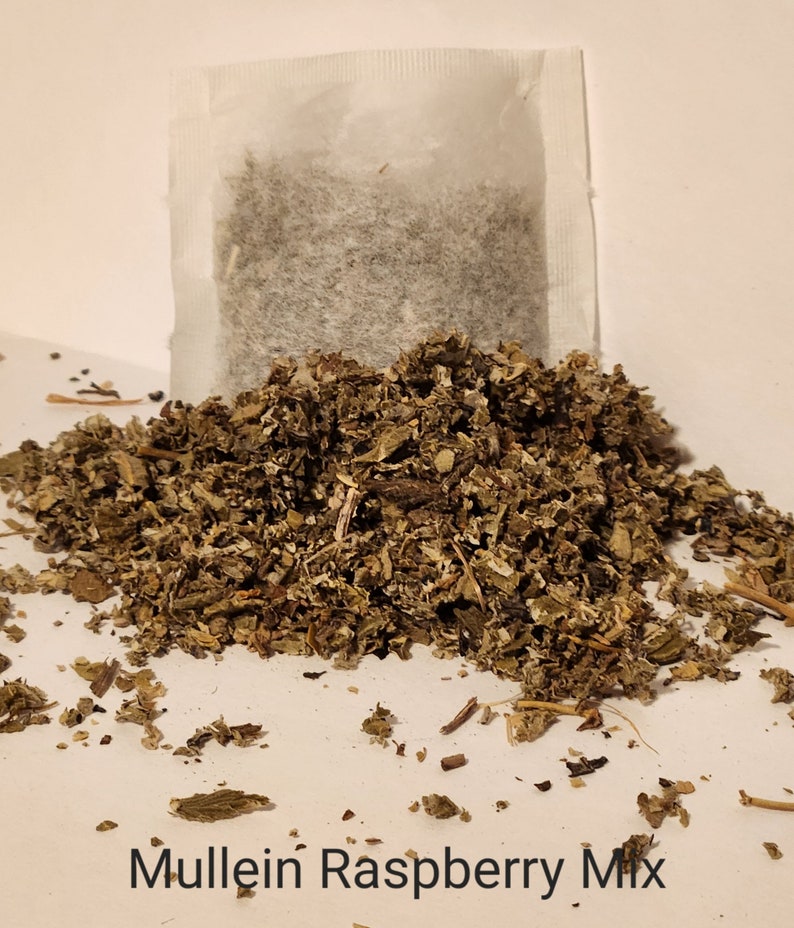 May include: A white tea bag filled with loose leaf tea sits on a pile of dried herbs labelled "Mullein Raspberry Mix".