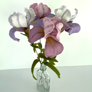 May include: A bouquet of purple and white felt irises in a clear glass bottle. The flowers are arranged in a vase with green felt leaves.