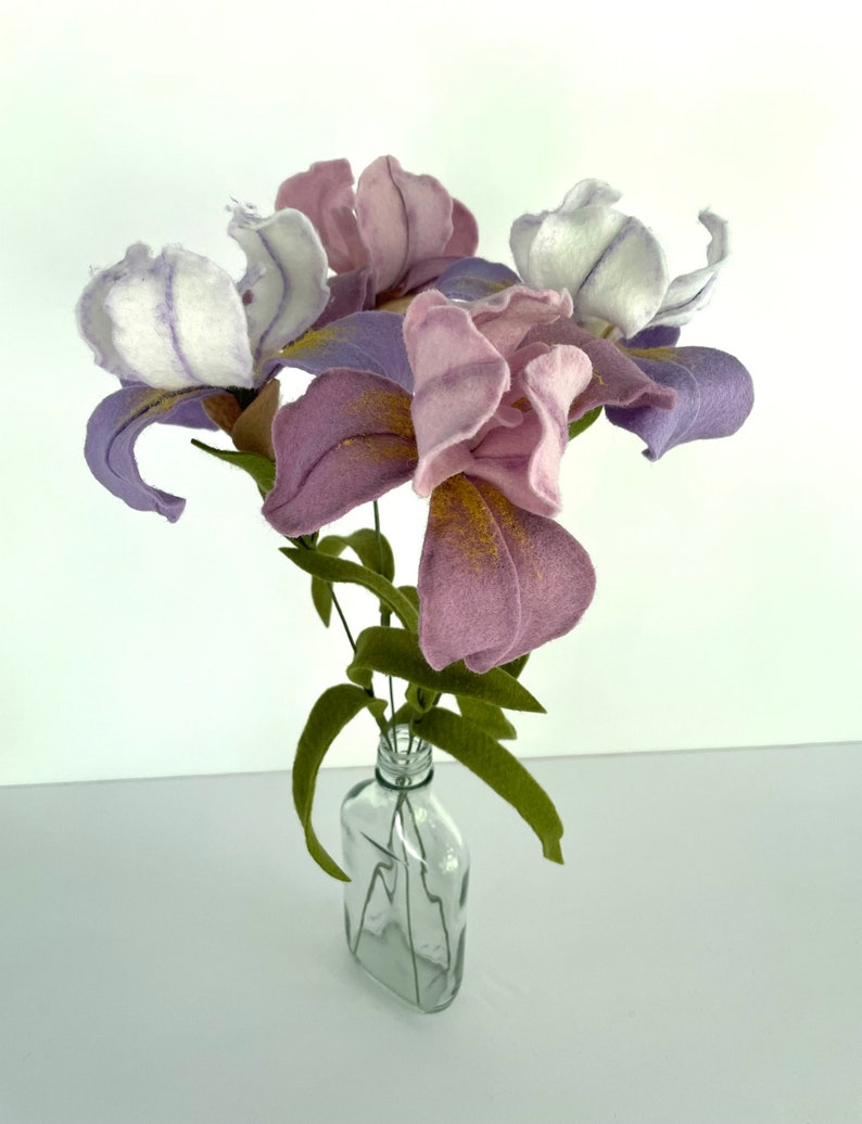 May include: A bouquet of purple and white felt irises in a clear glass bottle. The flowers are arranged in a vase with green felt leaves.