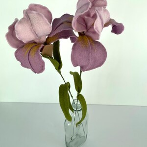 May include: A bouquet of three purple felt irises with gold accents in a clear glass vase.