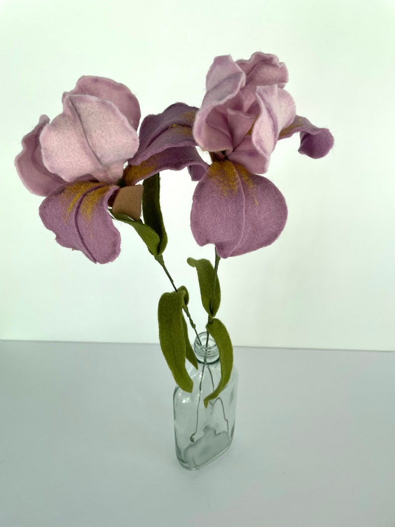 May include: A bouquet of three purple felt irises with gold accents in a clear glass vase.