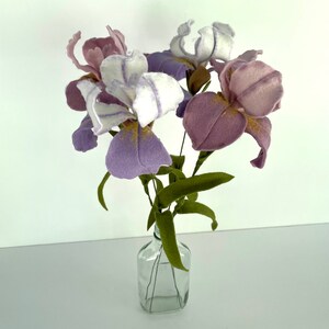 May include: A bouquet of purple and white felt iris flowers in a clear glass bottle. The flowers have a delicate, hand-crafted look.