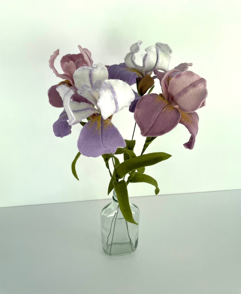 May include: A bouquet of purple and white felt iris flowers in a clear glass bottle. The flowers have a delicate, hand-crafted look.