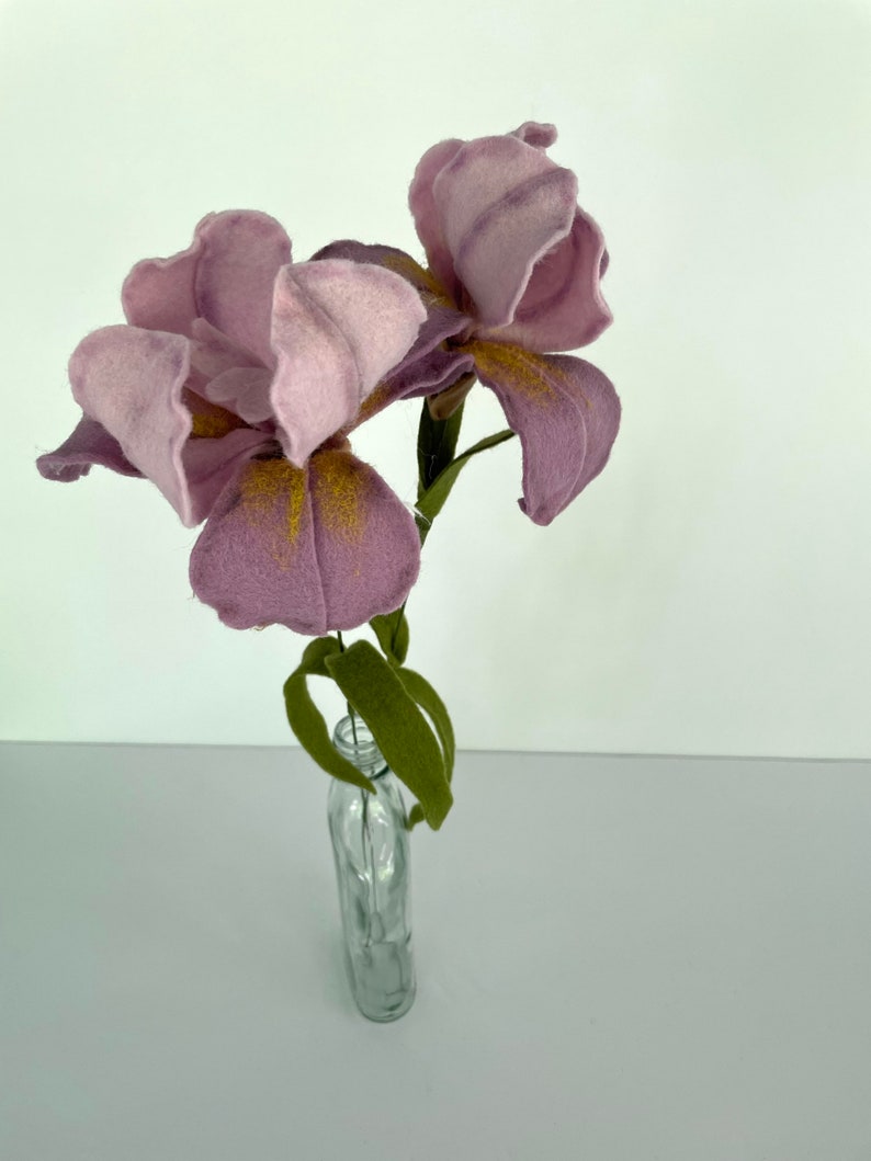 May include: Two purple felt iris flowers with yellow centers in a clear glass vase.
