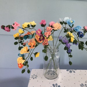May include: A bouquet of felt flowers in a variety of colors, including pink, yellow, blue, and purple, arranged in a clear glass jar.