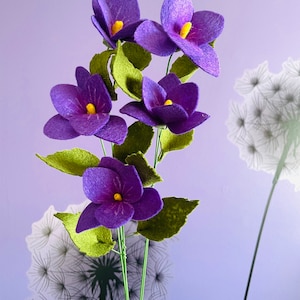 May include: A bouquet of five purple felt flowers with yellow centers and green felt leaves. The flowers are arranged on green wire stems.