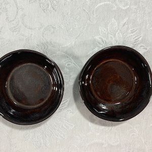 May include: Two dark brown ceramic bowls with a glossy finish. The bowls are empty and have a slightly uneven rim.