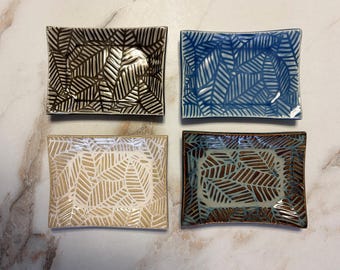 May include: Four rectangular ceramic dishes with a leaf pattern. The dishes are in shades of brown, blue, beige, and green.