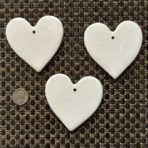 May include: Three white ceramic heart-shaped ornaments with a hole at the top for hanging.
