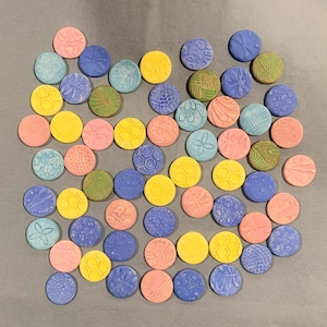 May include: A collection of colorful ceramic tiles with various patterns and designs. The tiles are round and have a glossy finish. They are arranged in a circular pattern on a gray background.