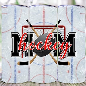 May include: A tumbler with a hockey-themed design. The design features the word "MOM" in black and white block letters with "hockey" in red script. A hockey puck, sticks, and a net are also included.