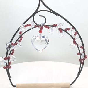May include: A black metal bird swing with a wooden perch and crystal heart hanging from red beads.