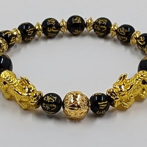 May include: Black and gold bracelet with Chinese characters and two gold lion charms.