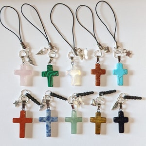 May include: Ten different cross charms made of various stones, including turquoise, malachite, and rose quartz. Each charm is attached to a black string with a silver connector and a decorative charm. The charms are arranged in two rows of five.