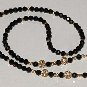 May include: A black beaded necklace with gold accents and three gold and crystal beads. The necklace has two clasps.