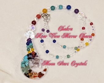 Puede incluir: Un collar de cristal de chakra arcoíris con un dije en forma de media luna. El collar está hecho con cristales transparentes y piedras de colores. El dije está hecho con una variedad de cristales y tiene un diseño de espiral plateado. El texto "Chakra Rear View Mirror Charm" y "Moon Stars Crystals" es visible en la imagen.