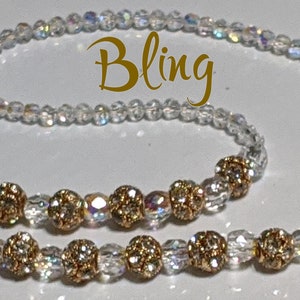 May include: A clear crystal beaded chain with gold-toned beads and two gold-toned clasps. The chain is labeled "Bling".