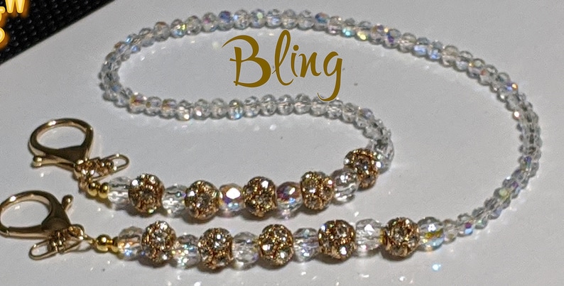 May include: A clear crystal beaded chain with gold-toned beads and two gold-toned clasps. The chain is labeled "Bling".