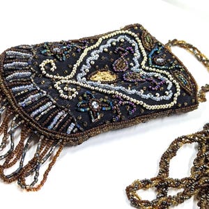 May include: A black beaded evening bag with a long strap. The bag is rectangular with a curved bottom edge and features intricate beadwork in shades of brown, gold, and iridescent colors. The bag has a fringe of brown beads.