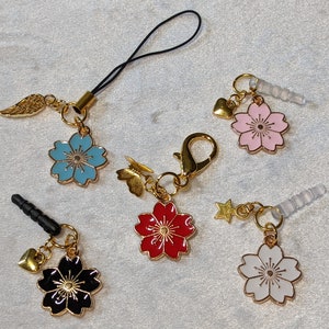 May include: Five gold-tone charm pendants featuring different colored flower designs. The charms are attached to black string, clear plastic earbud holders, and gold chains.