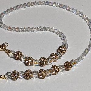 May include: A gold chain with clear and gold beads, featuring two gold clasps. The chain is designed to hold a mask or glasses.