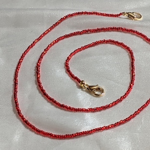 Puede incluir: Un collar de cuentas rojas con cierres dorados. El collar está hecho de cuentas pequeñas y redondas y mide aproximadamente 76 cm de largo.