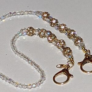 May include: A white beaded chain with gold accents and two gold clasps. The chain is made of small, iridescent beads and has a delicate, feminine look.