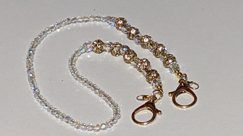 May include: A white beaded chain with gold accents and two gold clasps. The chain is made of small, iridescent beads and has a delicate, feminine look.