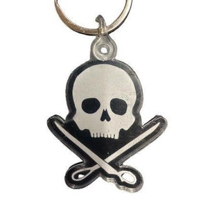 May include: A black and white skull and crossbones keychain. The skull is white with black eyes and a black background. The crossbones are silver.