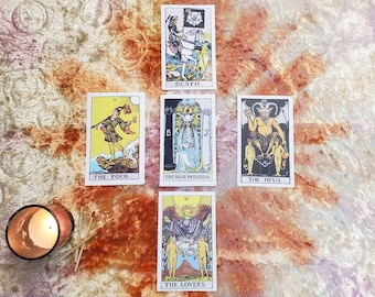 May include: Tarot card reading spread with ten cards, including The Fool, The High Priestess, The Devil, Death, and The Lovers. The cards are laid out on a textured surface.