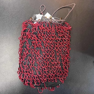 May include: A small, black handbag with a red, looped beaded overlay. The bag has a drawstring closure and a twisted cord handle. The red beading creates a textured, decorative pattern across the surface of the bag.
