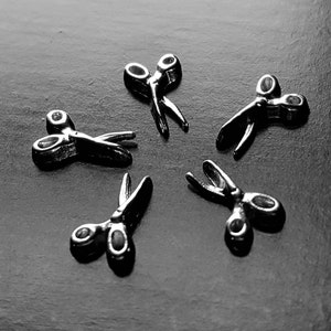 May include: Six silver scissors arranged in a circular pattern on a dark gray surface.