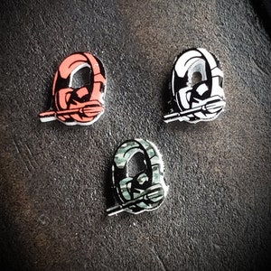 May include: Three small, round, ceramic pins with a black and white design of a helmet with a spear. The pins are in red, white, and green.