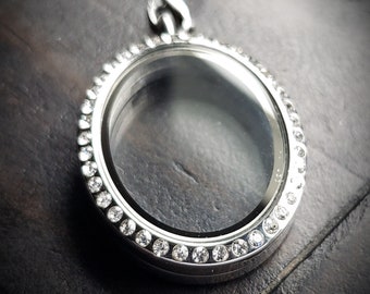 May include: A silver locket necklace with a clear glass insert and a row of clear rhinestones around the edge.