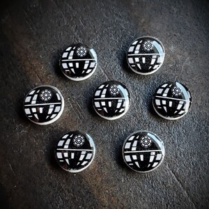 May include: Seven black and white round buttons with a white image of the Death Star from Star Wars.