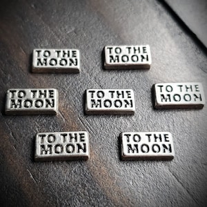 May include: Eight silver metal charms with the text "To the Moon" on each charm.