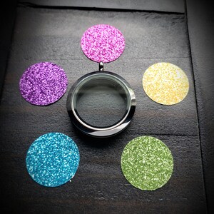 May include: A silver locket charm with a clear glass insert, surrounded by five glitter-covered circles in pink, purple, yellow, blue, and green.