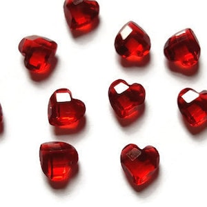 May include: Ten red heart-shaped glass beads on a white background.