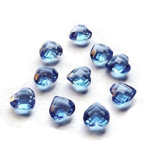 May include: Ten blue heart-shaped glass beads. The beads are faceted and have a light blue color.
