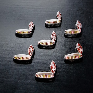 May include: Seven silver-toned pins with red and yellow enamel designs. Each pin features a stylized headdress with a feather.