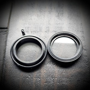 May include: Two black metal locket pendants with clear glass inserts. The locket on the left has a loop for attaching a chain.