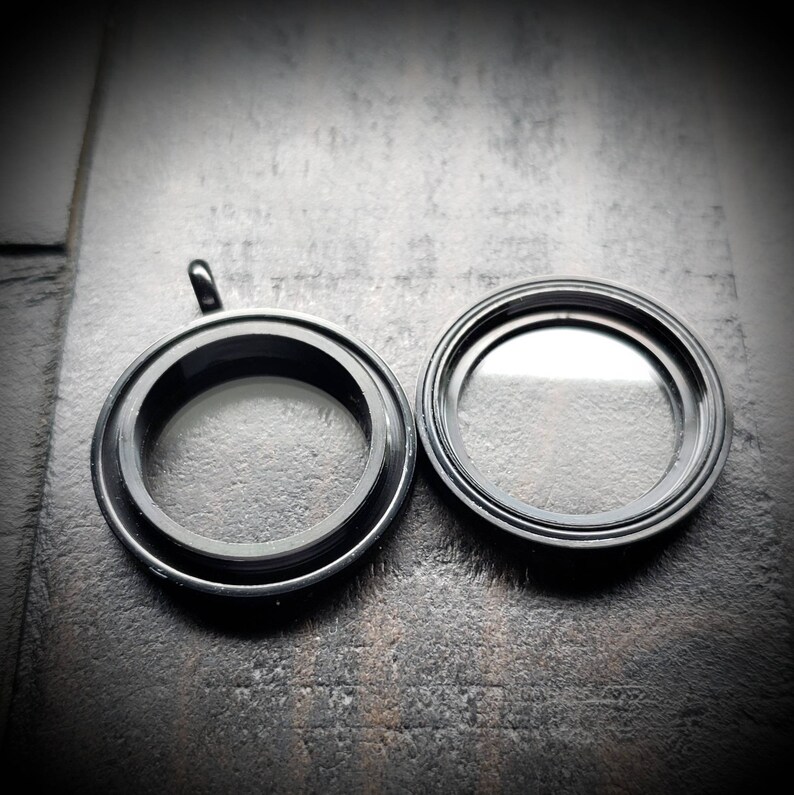 May include: Two black metal locket pendants with clear glass inserts. The locket on the left has a loop for attaching a chain.