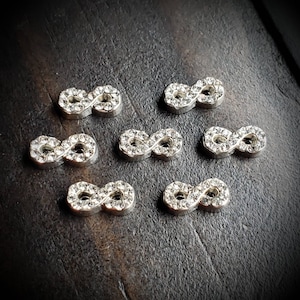 May include: Eight silver infinity charms with clear rhinestones. Each charm is about 1 inch long.