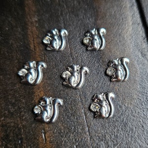 May include: Seven silver squirrel charms with clear rhinestones. Each charm features a squirrel holding a nut.