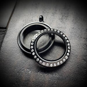 May include: Black locket with a clear glass insert and a row of clear rhinestones around the edge.