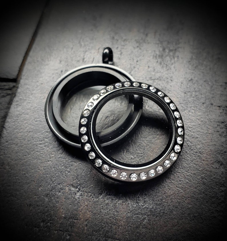May include: Black locket with a clear glass insert and a row of clear rhinestones around the edge.