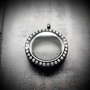 May include: Black locket pendant with a clear glass insert and a border of small clear rhinestones.