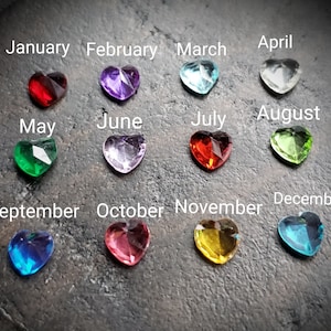 May include: A collection of heart-shaped gemstones in various colors, each labeled with a month of the year. The gemstones include red, purple, blue, clear, green, and yellow. The text labels are in white.