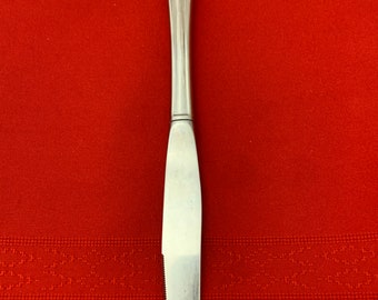 May include: A silver dinner knife with a fluted handle. The knife is on a red tablecloth.