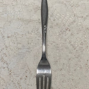 May include: A silver fork with a simple design. The fork has a long, slender handle and four prongs.